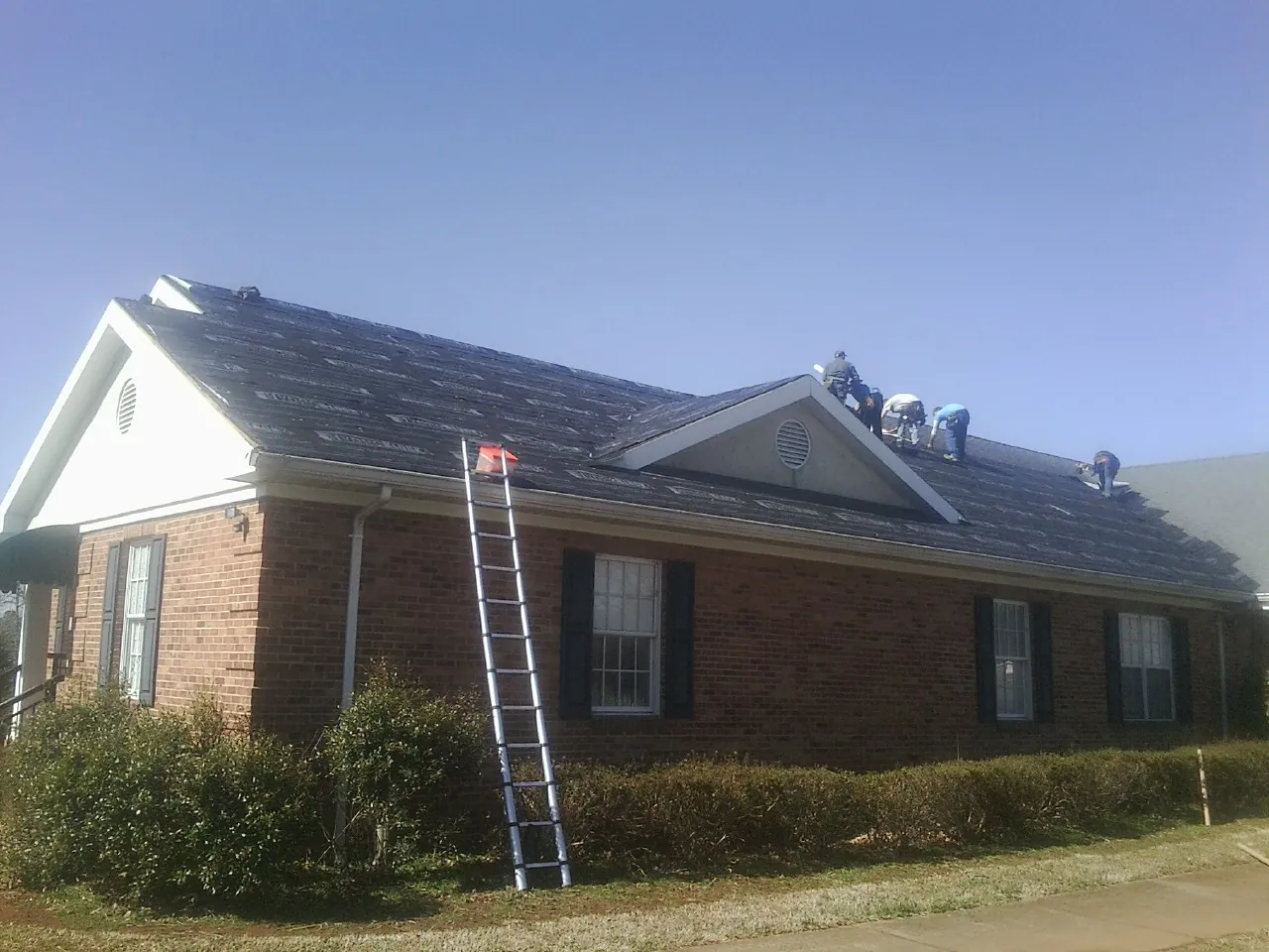 Crew tearing shingles off a brick ranch roof with a ladder set — Emergency Roof Repair work by our crew in Mililani