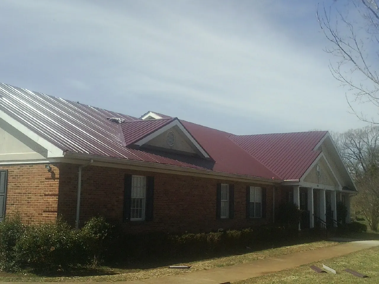 Red metal roof with gabled entries on a long brick building, from a Hail Damage Roof Repair job in Mililani