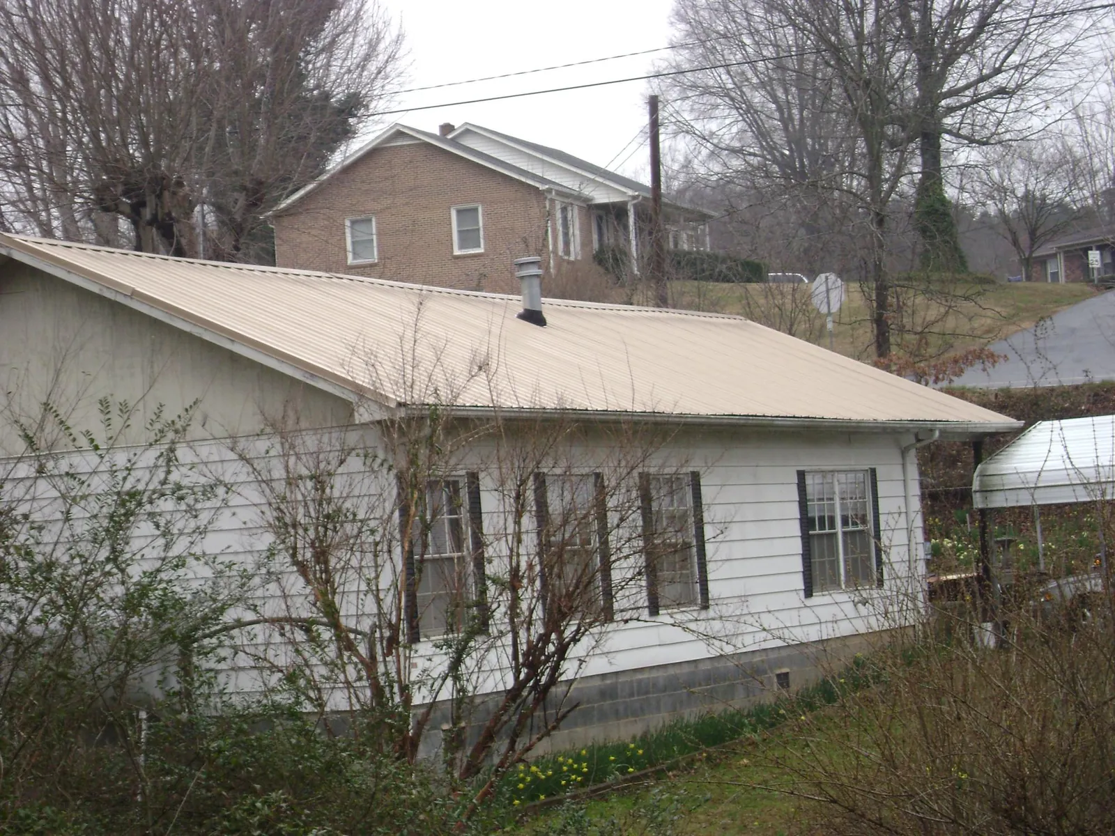 Tan metal roof on a white sided house set into a hillside — Commercial Roofing by Roofing Brothers in Mililani